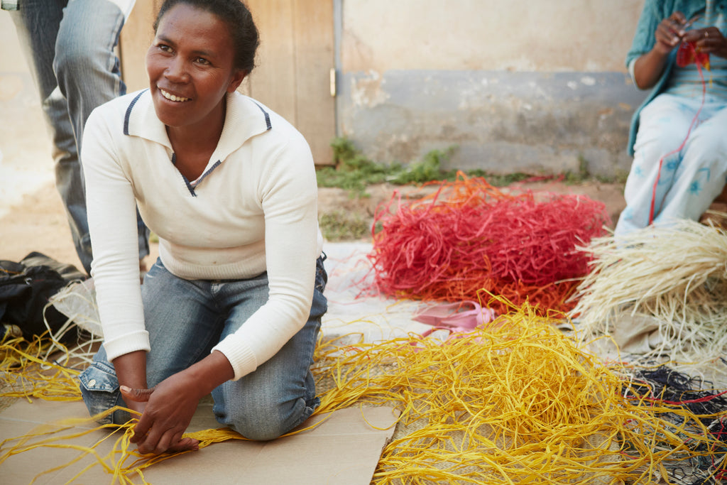 Woman in Madagascar working with assorted piles of colored raffia