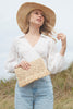 Model on a grassy background holding the Denise clutch in Natural