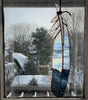 Stained glass feather with white and blue panes hanging from leather tie in window