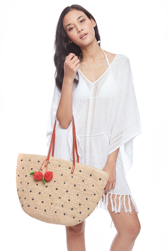 Model holding Florence crocheted raffia tote with cherry poms and navy polka dots