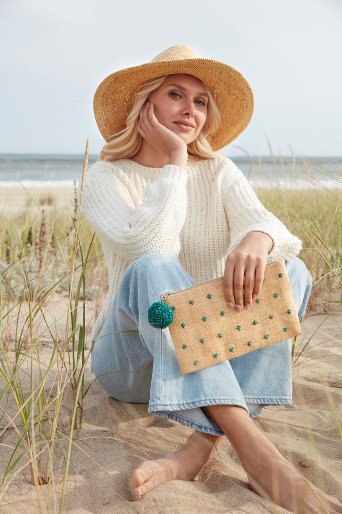 Model holding natural woven zip pouch with aqua colored stars and pom pom