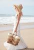 Model wearing natural colored fringed raffia sun hat with braided tie and sand Samana tote