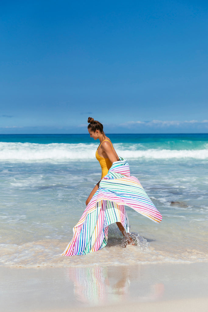Model wearing rainbow striped beach blanket