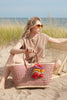 Model sitting in the sand with our Madrigal tote in Pink
