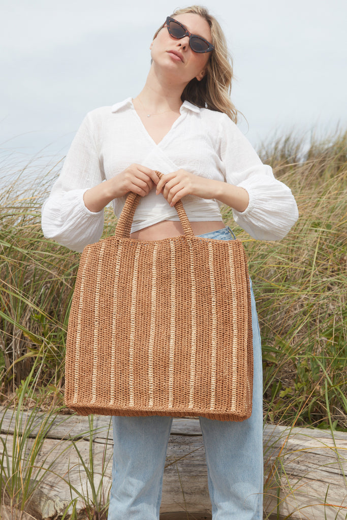 Model holding Marbella tote in Sand with Natural stripes in front of grassy background