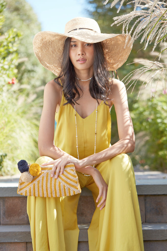 Model holding sunflower and natural colored striped crocheted clutch with cotton lining, pom poms, and zip closure