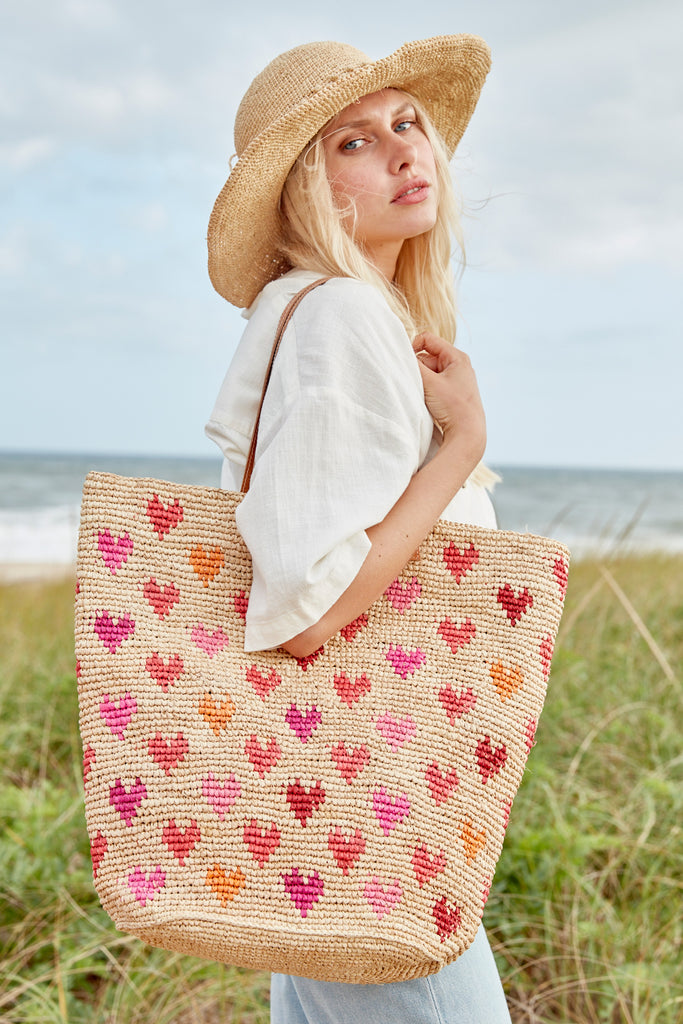 Model on the beach wearing our Stella raffia sun hat in Natural and our Amelie raffia tote in Pink Multi