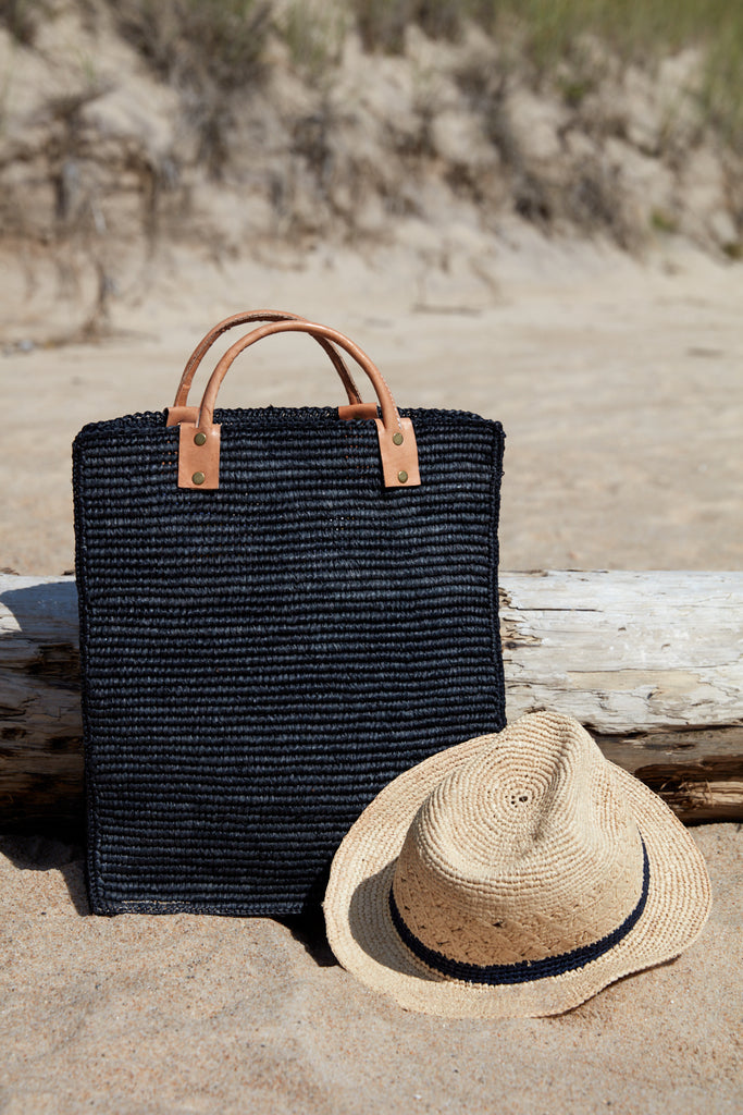Marcel tote in black and a hat in the sand