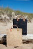 Marcel tote in Black and Natural sitting on a beach log