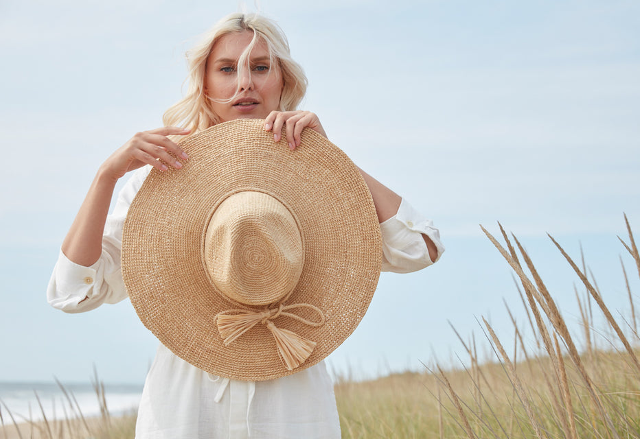 Model holding our Jane Natural hat in a beach setting