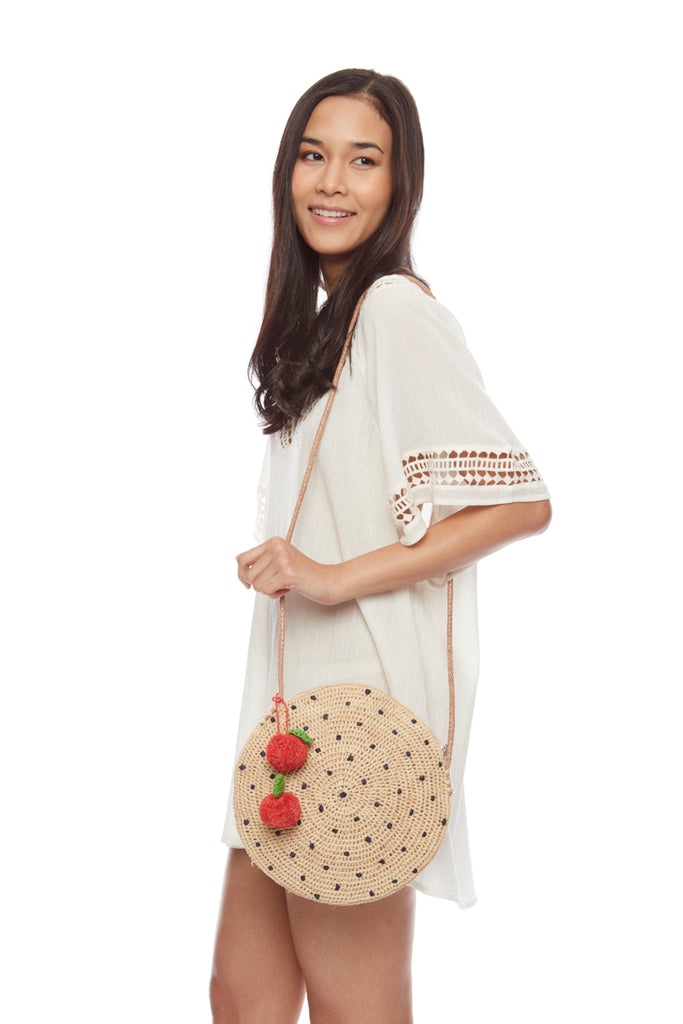Model with navy colored polka dot crocheted shoulder bag with leather strap, and cherry pom poms