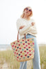 Model holding Amelie crocheted carryall with multi colored heart pattern on the beach.