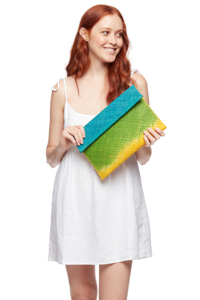 Model holding ocean, apple, sunflower colored ombre woven clutch with cotton lining and snap closure