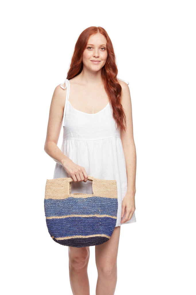 Model holding variegated navy colored crocheted raffia tote with inside pocket and snap closure
