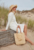 Model holding natural colored crocheted north-south tote with cotton lining, leather straps & removable tassel