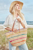Model on the beach wearing our Cielo raffia tote in Natural and our Mika raffia sun hat in Natural