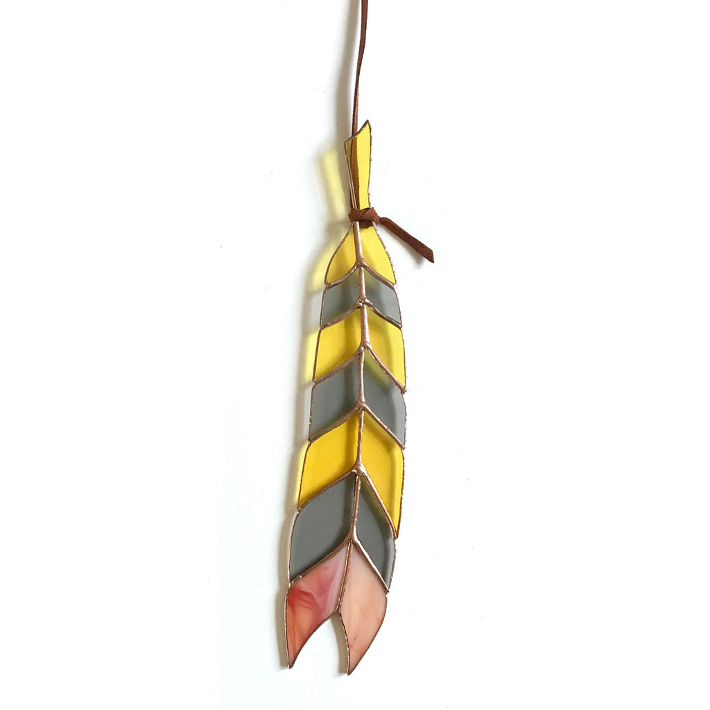 Stained glass feather with yellow, gray, and pink panes hanging from leather tie