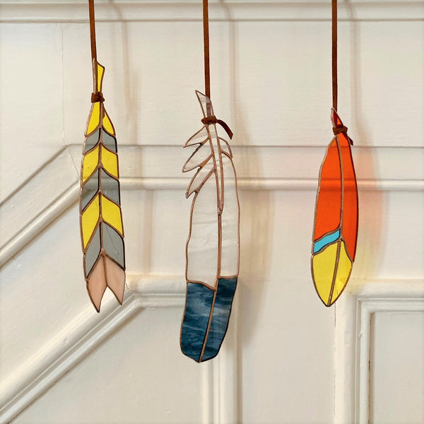 Three different stained glass feathers hanging from leather ties