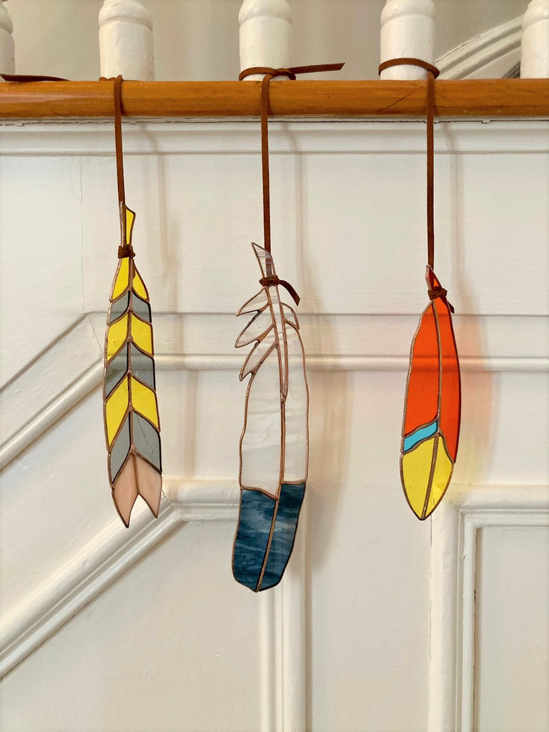 Three stained glass feathers hanging from leather ties