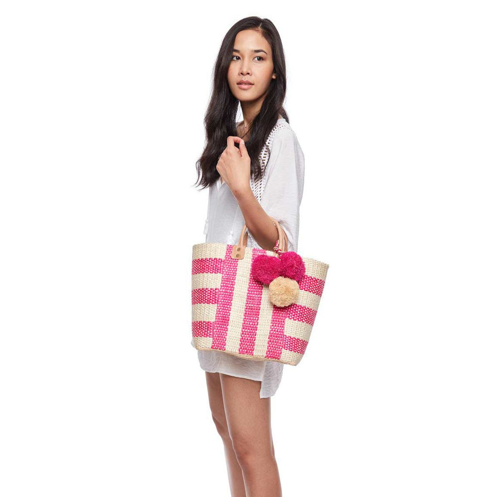 Model holding pink striped woven sisal basket tote with pom poms and leather handles
