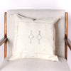 Cream colored square pillow with embroidered design on a chair