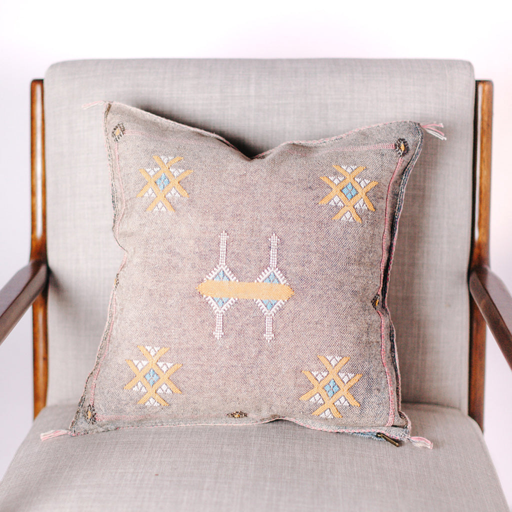 Dove colored square pillow with embroidered design on a chair