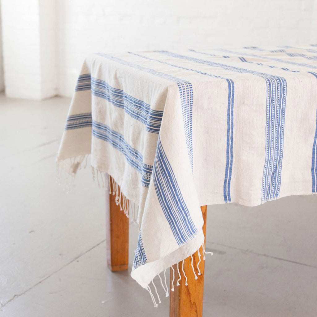 Handspun white tablecloth with blue stripes on a wood table