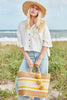 Model on the beach wearing our Stella raffia sun hat in Natural and our Cyprus sisal beach tote in Sunflower