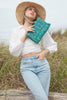 Model on a grassy background holding Denise clutch in Aqua