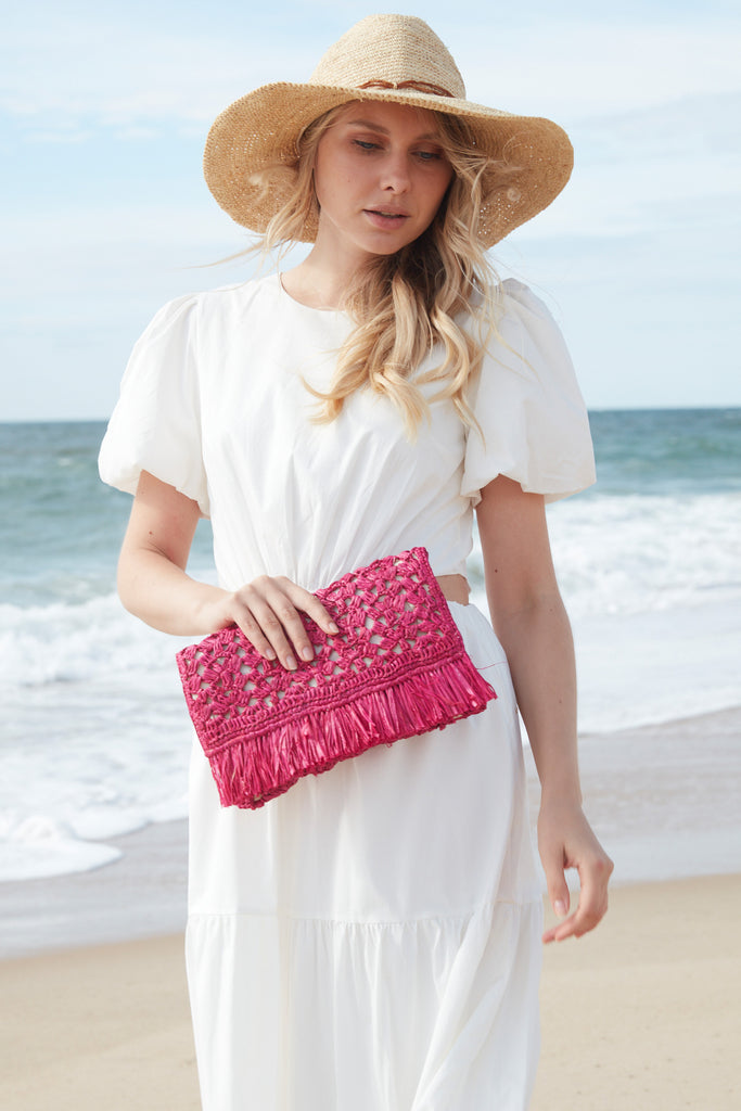 Model on a beach holding the Denise clutch in Pink
