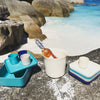 Blue and white and aqua plates and cups and trays arranged on a rock with a wine bottle