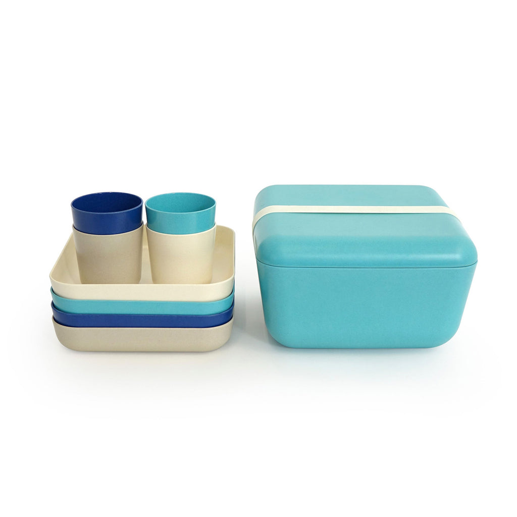 Blue and white and aqua plates and cups and trays stacked next to closed carrying case