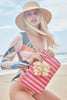 Model sitting on beach with Esme clutch in pink