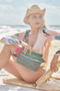 Model on a beach chair wearing our Rose Sun hat in Natural and our Evie clutch in Aqua