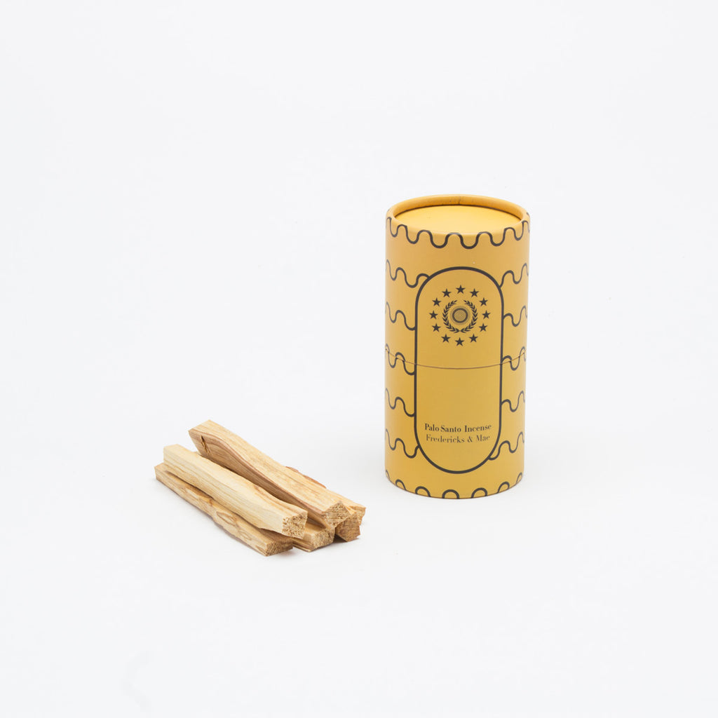 Palo Santo incense in a pile next to it's yellow tube container