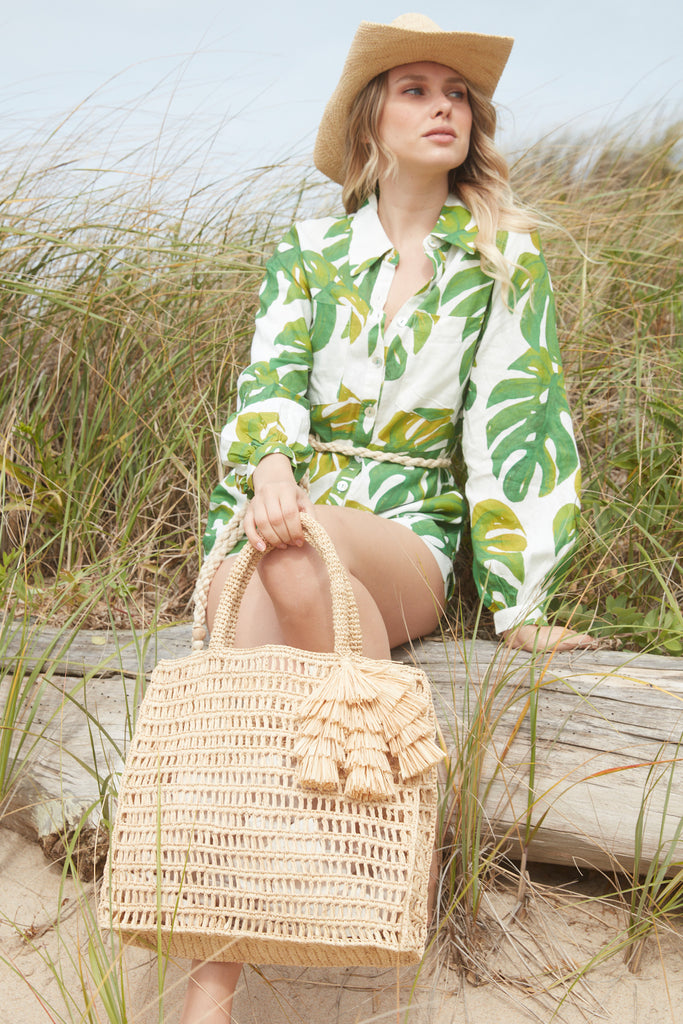 Model sitting on a beachy log holding the Georgia tote in Natural