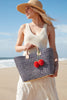 Model on the beach wearing our Stella raffia sun hat in Natural holding our Hadley beach tote in Navy
