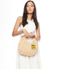 Model holding natural colored crocheted raffia clutch with wooden handles, cotton lining, and pineapple charms