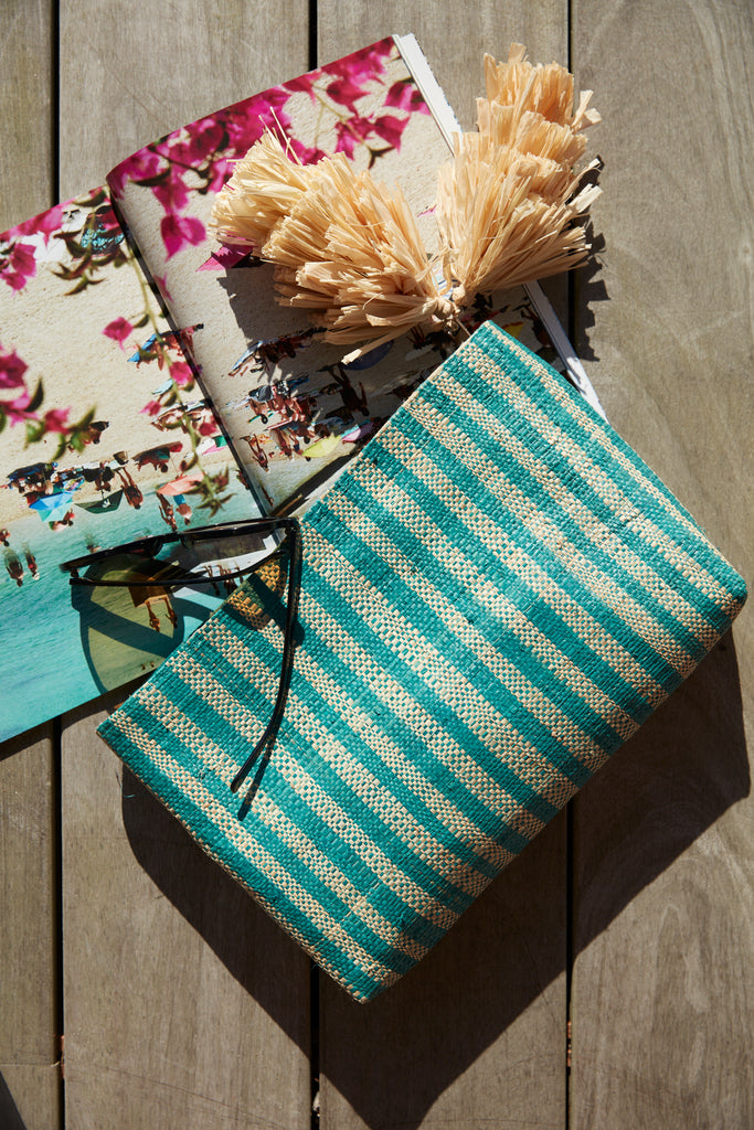 Esme clutch in Aqua on a deck with a magazine and sunglasses