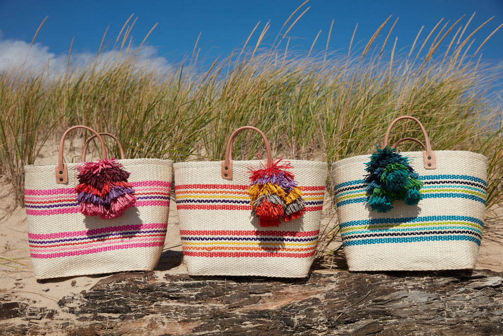 Caracas totes in Pink Multi, Coral Multi and Aqua Multi sitting on a grassy log