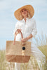 Model holding color block sand colored crocheted carryall with leather straps & raffia pom poms