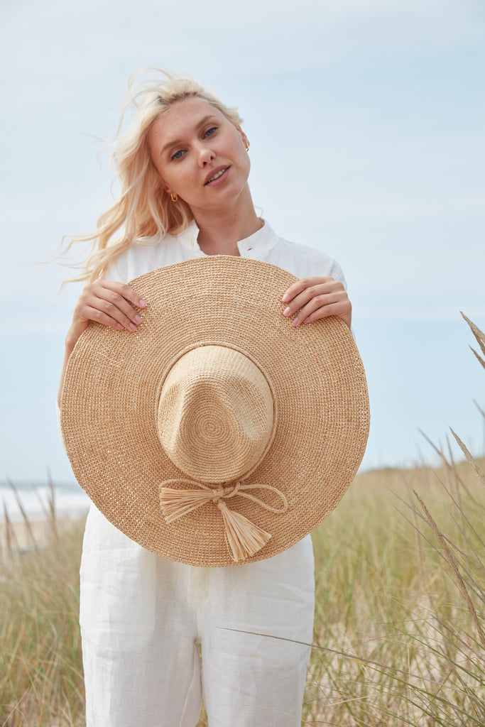 Model holding natural crocheted wide brim sun hat with raffia cord