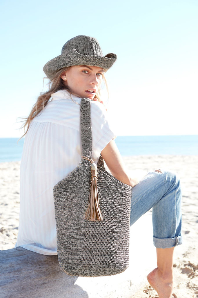 Model holding dove colored crocheted raffia shoulder bag with leather tassel & snap closure