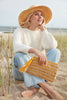 Model holding sunflower colored striped crocheted raffia zip pouch with zipper and raffia tassel