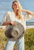 Model on the beach holding our Jessa raffia sun hat in Dove