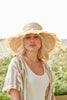 Model wearing natural colored fringed raffia sun hat with braided tie