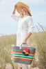 Model holding dove colored, multi-colored striped basket tote with removable tassels and leather handles