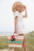 Model holding natural colored, multi-colored striped basket tote with removable tassels and leather handles
