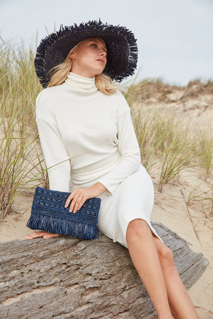 Model holding navy colored crocheted fringe clutch with cotton lining and snap closure