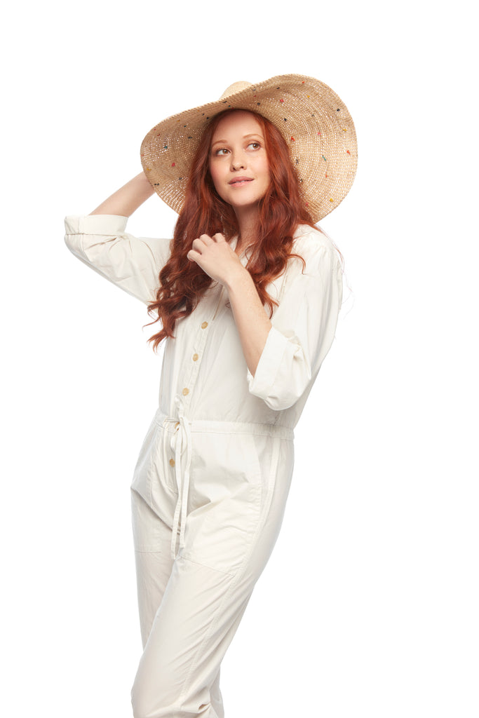 Model wearing wide brimmed raffia sun hat with multi colored embroidered polka dots and braided cord